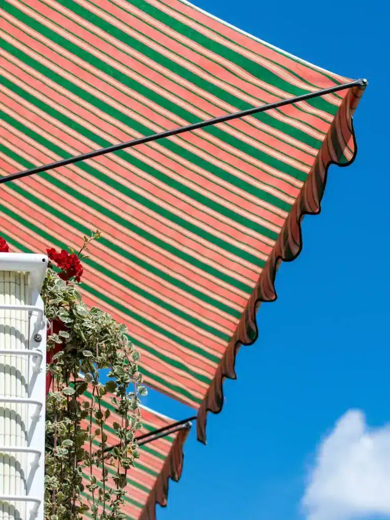 Store balcon rayé orange et vert offrant de l'ombre, avec un ciel bleu en arrière-plan.